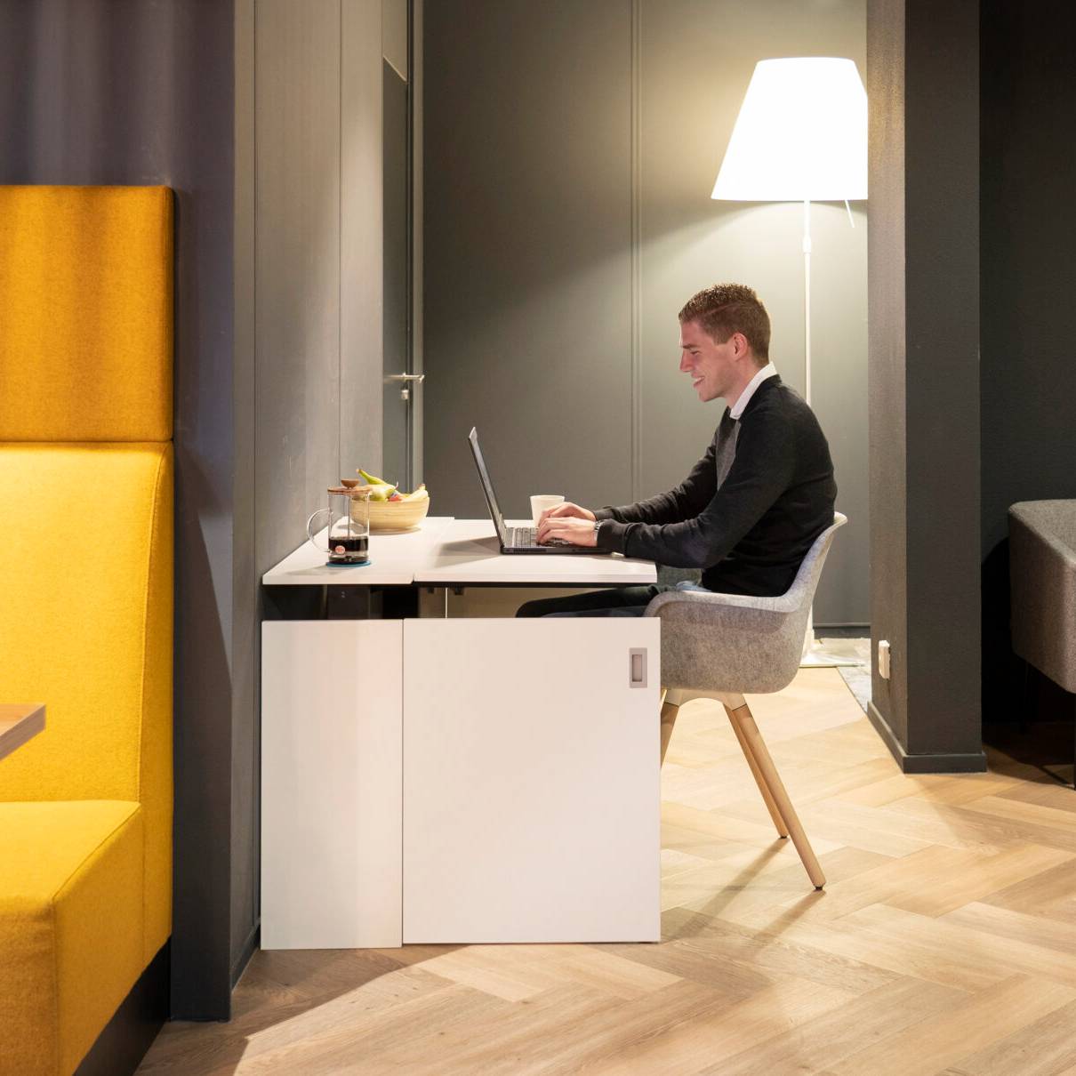 Een man werkt aan een bureau in een kamer, gebruikmakend van de HomeFit thuiswerkplek voor optimale ondersteuning.